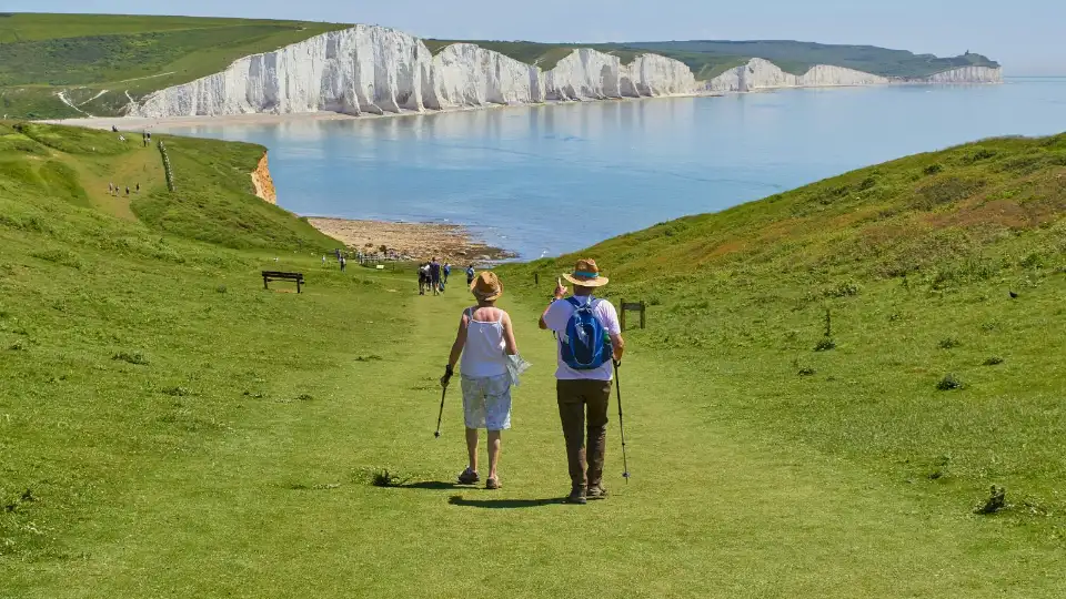 A couple walking a grassy coastal trail toward white cliffs